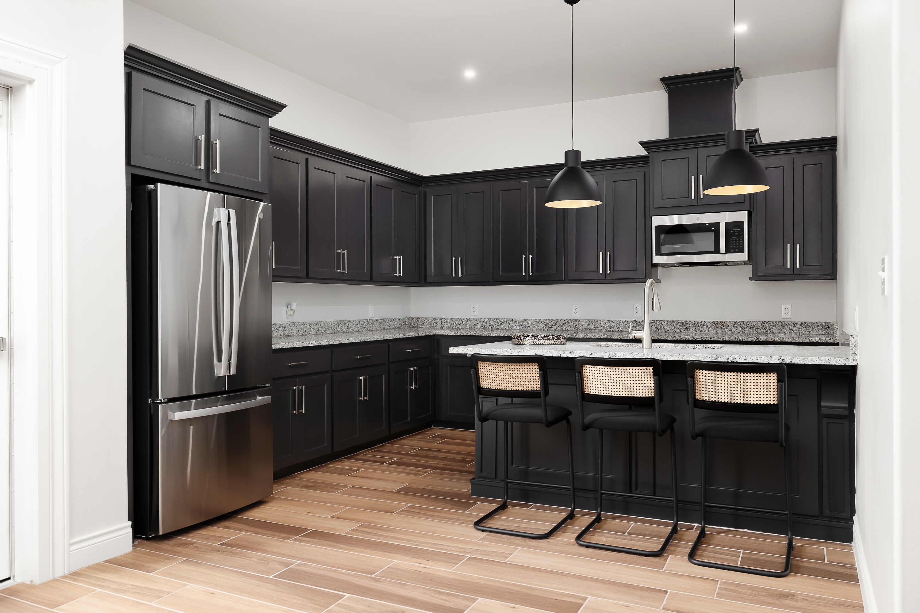 Modern kitchen with dark cabinetry, stainless steel refrigerator, and a granite-topped island with black bar stools.