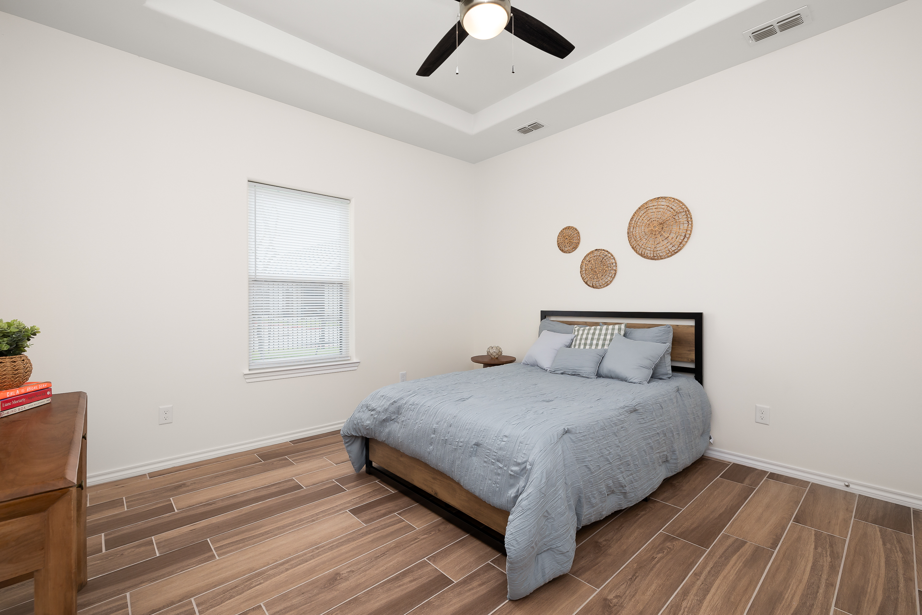 Bedroom with a low bed, gray quilt, and three round wicker wall decorations above the headboard on a beige wall.