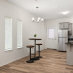 Bright open kitchen and dining area with gray cabinets, stainless steel fridge, and a round bar-height table with three stools near windows.