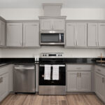 Modern kitchen with gray cabinets, stainless steel appliances, and black granite countertops across a U-shaped layout.