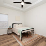 Bedroom with a metal-framed bed, beige bedding, mint throw, and a ceiling fan in a bright white room with a window and blinds. (informative)