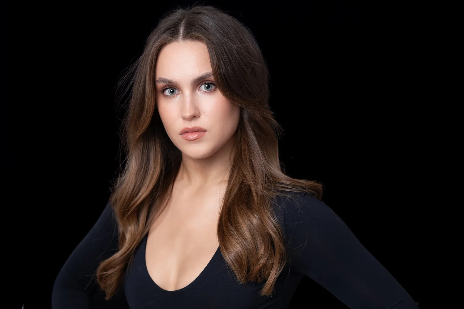 Portrait of a young woman with long brown hair and blue eyes against a solid black background.