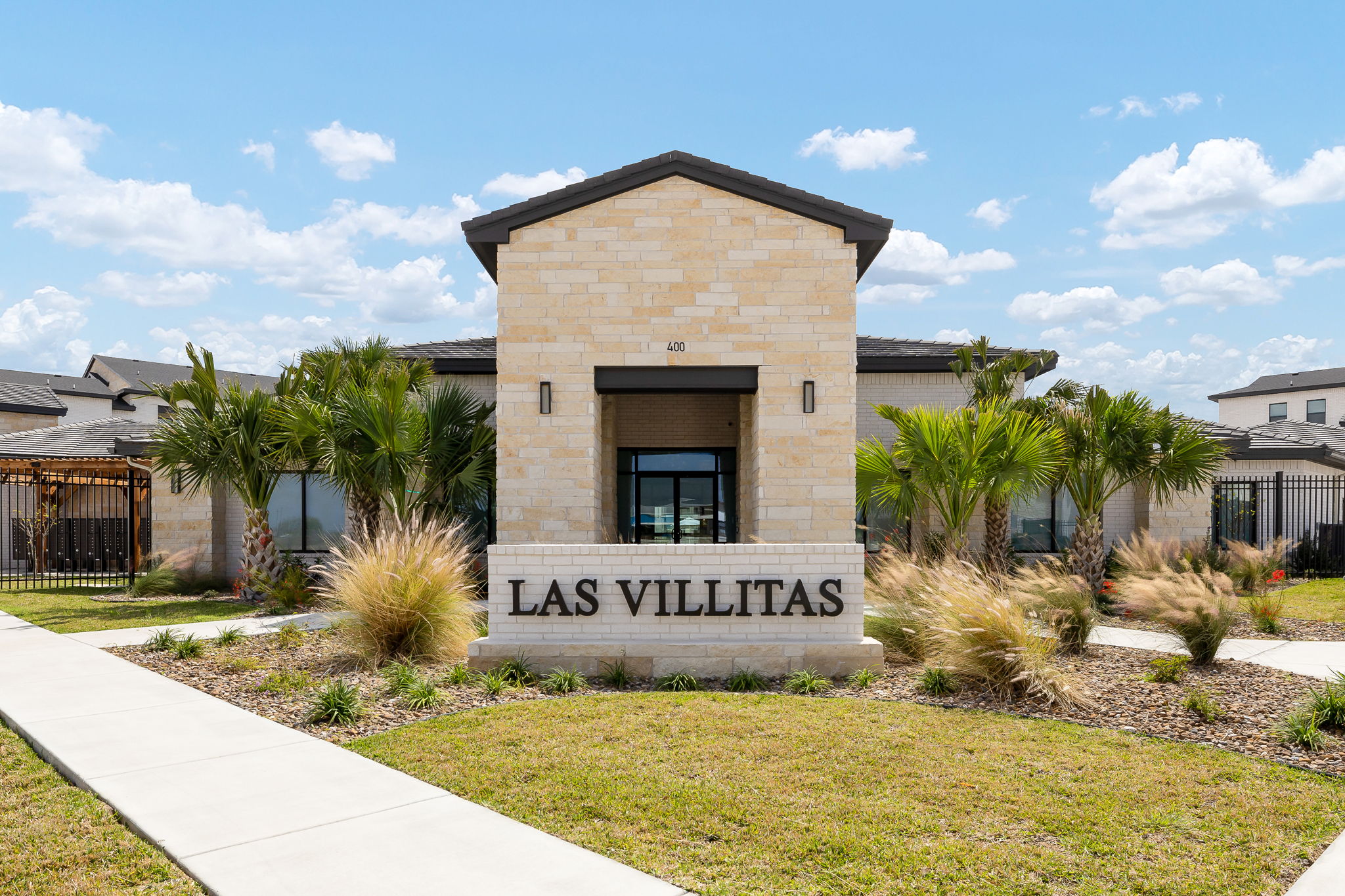 Stone entrance sign for Las Villitas housing community with palm trees and a blue sky.
