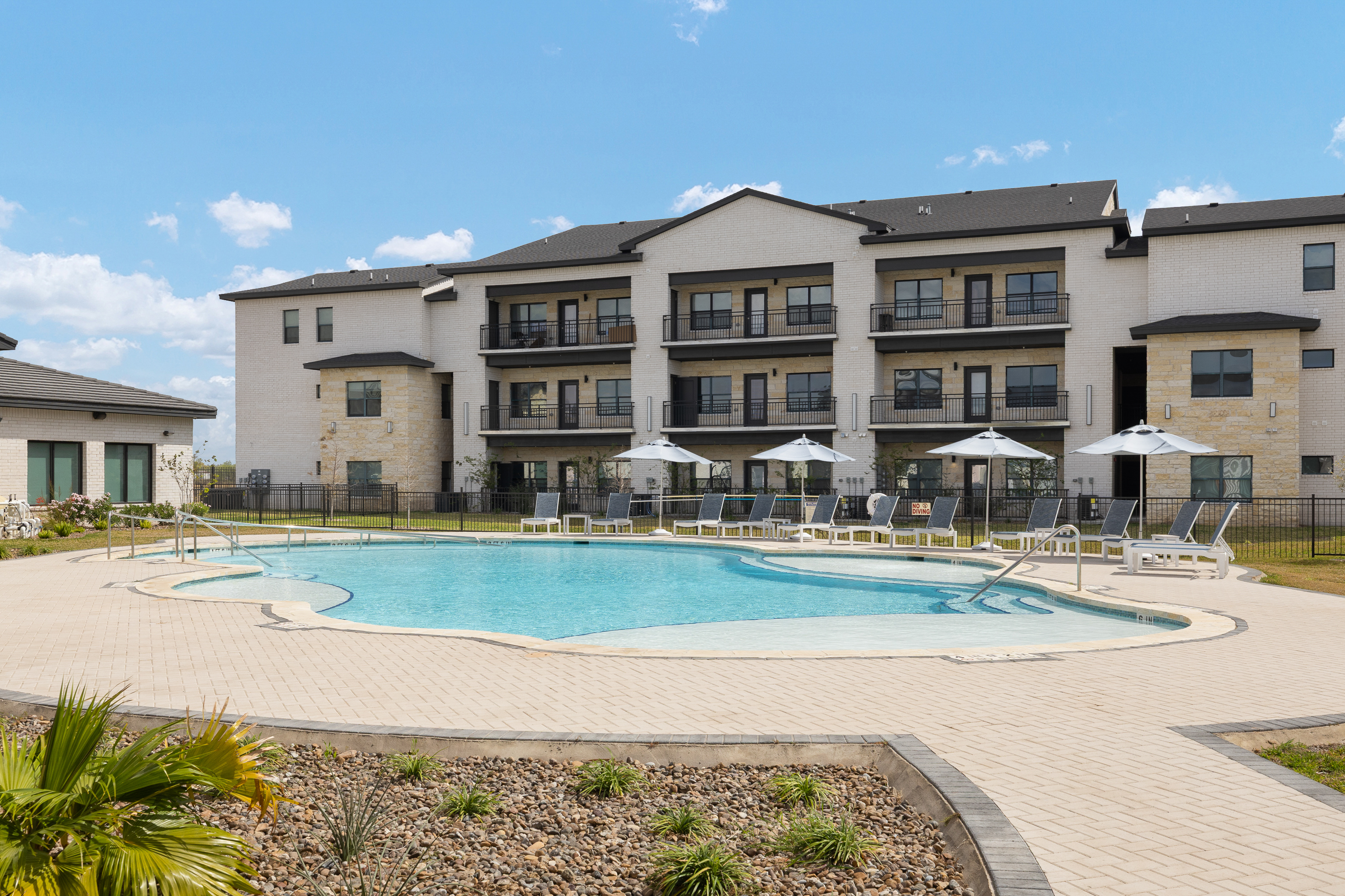 Modern apartment complex with balconies around a large outdoor pool and sun loungers under white umbrellas.