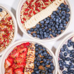 Parfait bowls topped with blueberries, banana slices, strawberries, and granola.