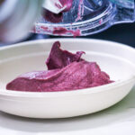 Purple ice cream being scooped into a white bowl from a dispensing container.