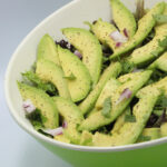 Bowl of avocado slices with red onion, greens, and herbs, seasoned with black pepper and herbs