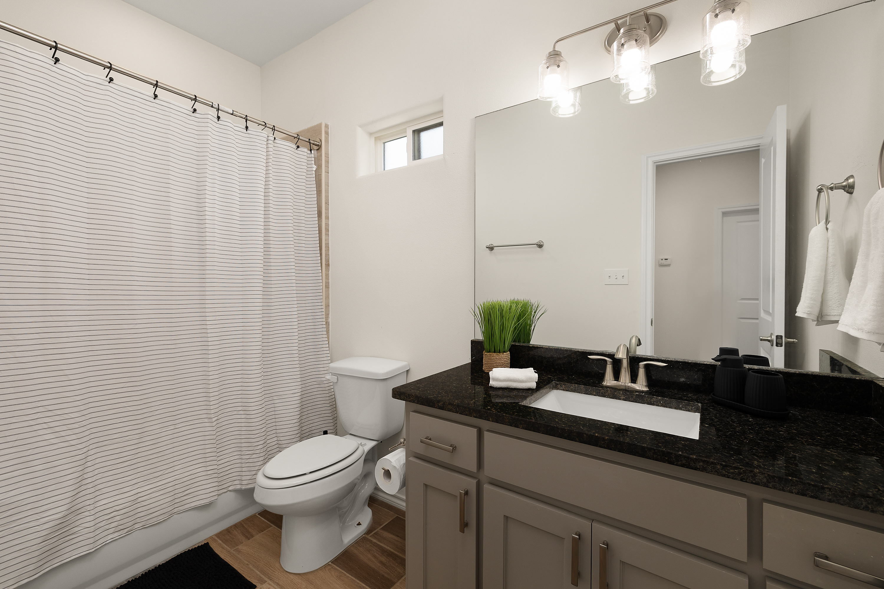 Bright, modern bathroom with a gray vanity, black granite countertop, large mirror, and trio of glass globe lights above.