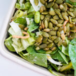 Leafy green salad topped with pumpkin seeds in a shallow dish