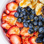 Fresh fruit bowl featuring sliced strawberries, blueberries, banana pieces and sprinkled cacao nibs