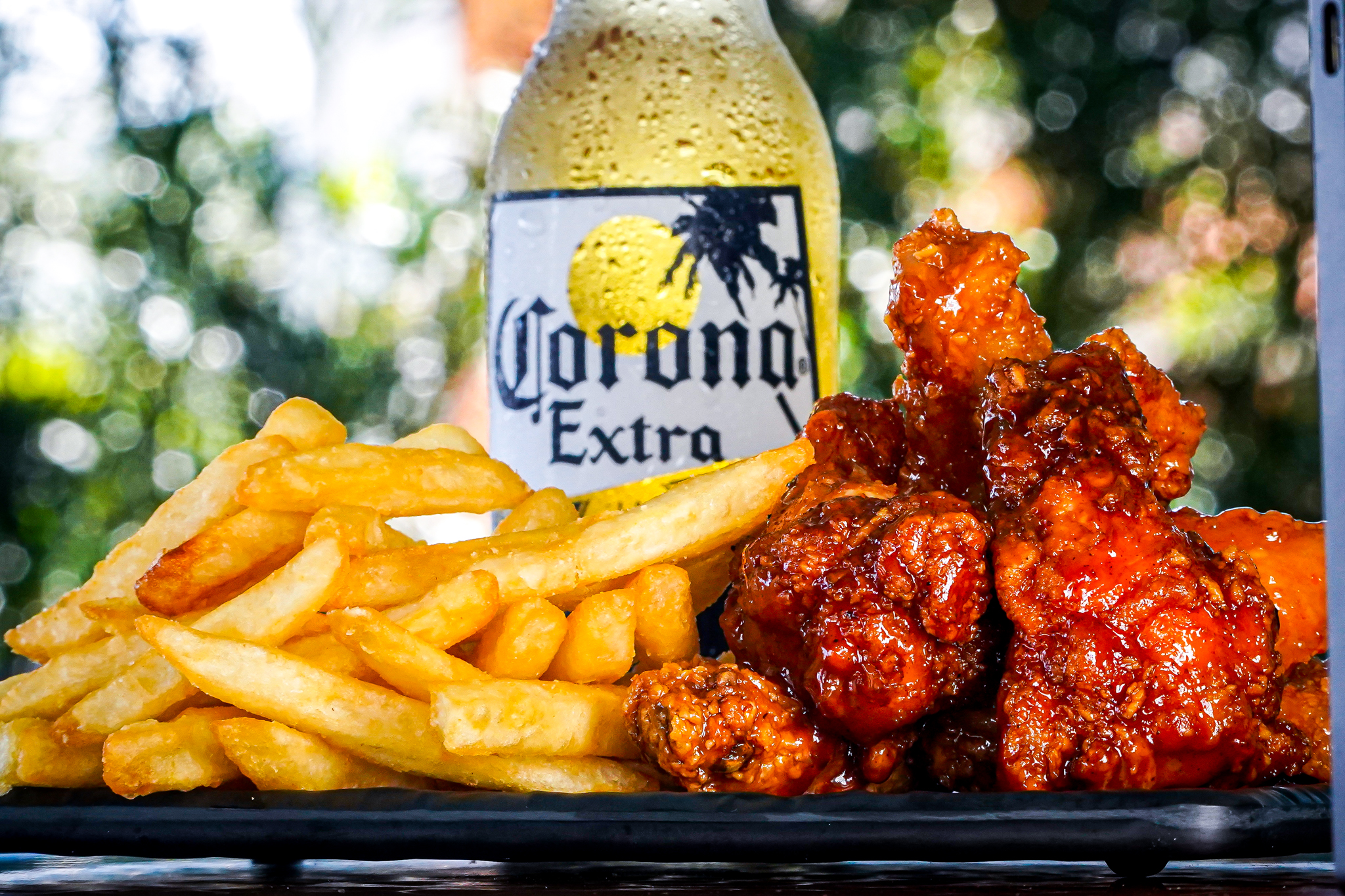 Corona Extra bottle flanked by a bed of golden french fries and saucy orange chicken wings on a serving platter