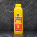 Yellow mango-lemonade drink bottle standing upright on a dark textured surface, labeled Tropibowls Mango Lemonade with a cartoon pineapple logo.