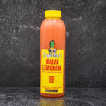 Orange bottle of TropiBowls guava lemonade with a yellow cap, set against a dark textured background on a black surface.