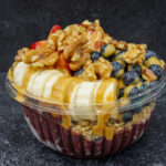 Dessert parfait in a clear cup with banana slices, blueberries, walnuts, granola, and caramel sauce drizzle.