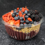 Parfait in a clear cup with granola layers and fresh berries (strawberries, blueberries, blackberries) on top.