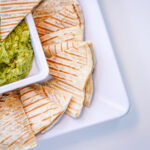 Creamy green guacamole in a white tray, surrounded by triangular tortilla chips for dipping.