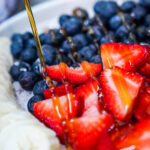 Close-up of a bowl with blueberries, sliced strawberries, banana, and a drizzle of honey on top.