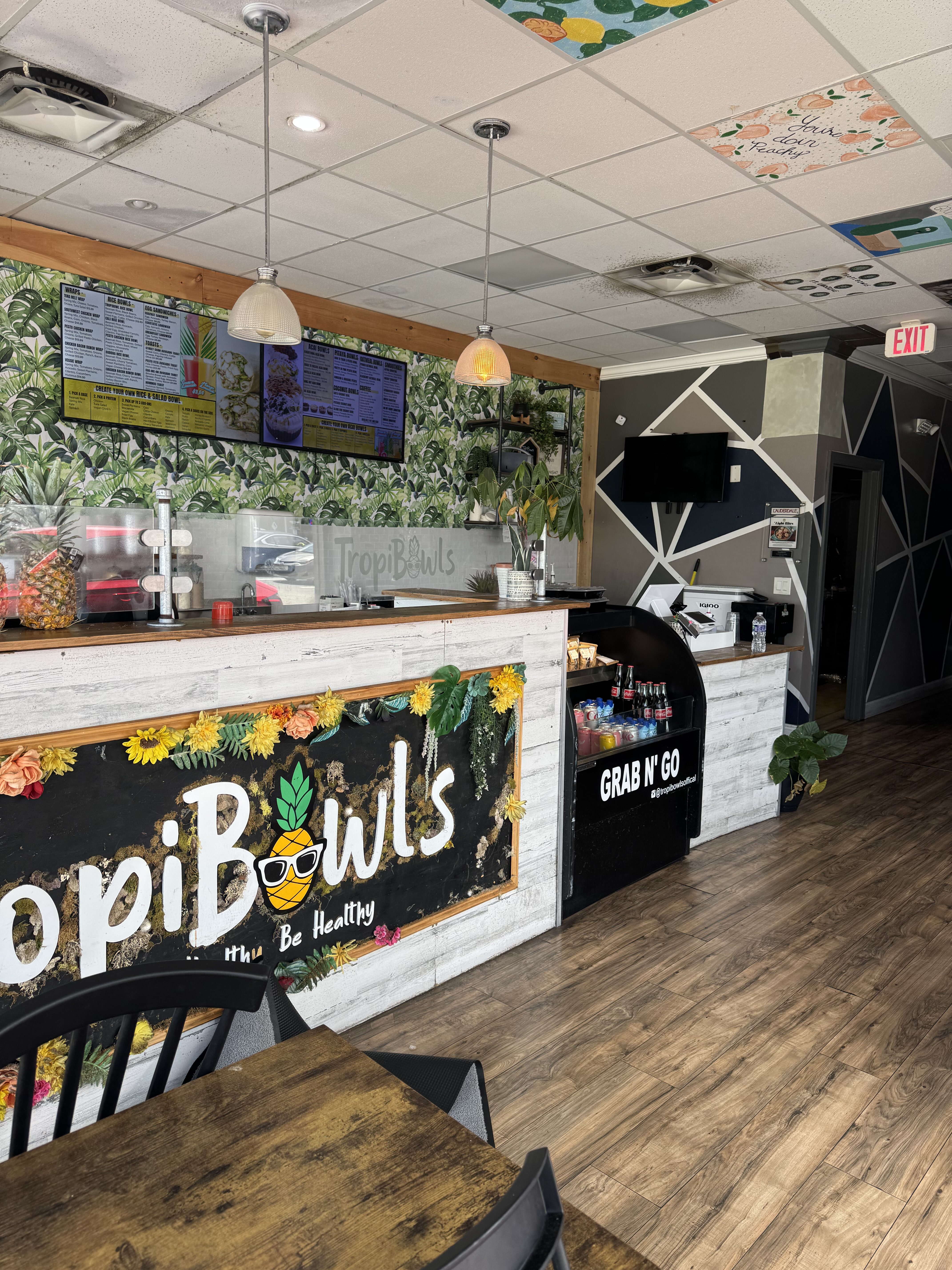 Interior of a tropical bowls cafe with a counter, menu boards, and a Grab N' Go cooler visible behind the bar area.
