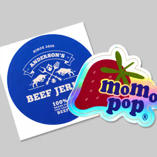 Two overlapping stickers: a blue round Anderson's Beef Jerky logo and a pink strawberry 'mom pop' sticker on a gray background.
