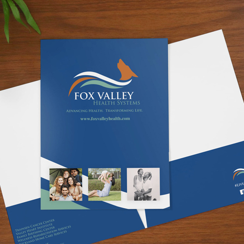 Blue Fox Valley Health Systems brochure on a wooden table, showing the logo, slogan 'Advancing Health. Transforming Life.', website, and four small photos at the bottom.