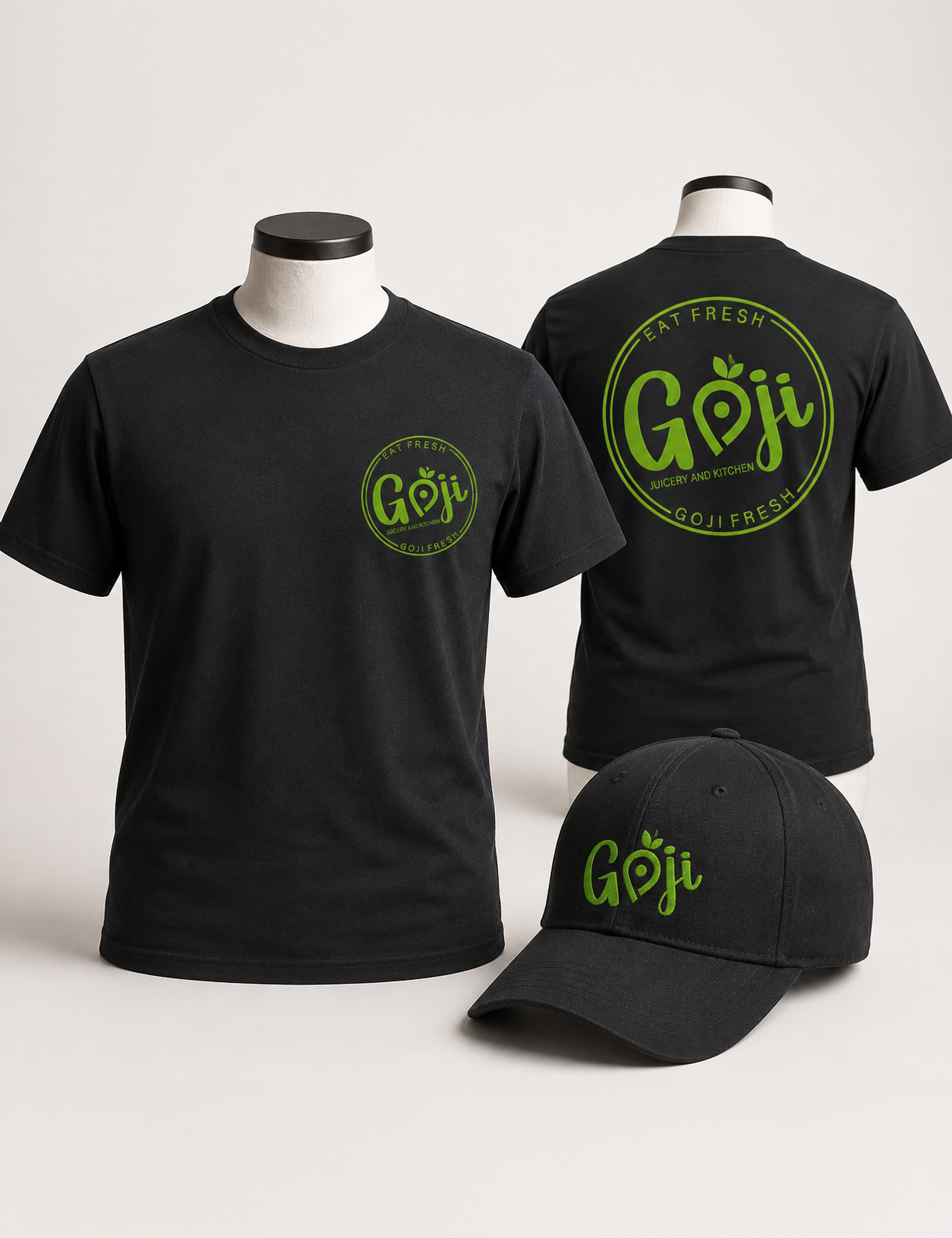 Black T-shirt with a small green Goji logo on the chest and a large Goji Fresh emblem on the back; matching Goji-branded cap nearby.