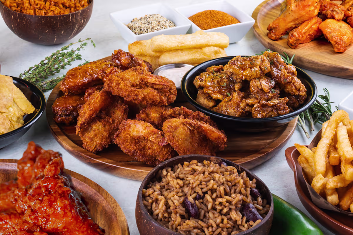 Assortment of fried foods and sides on wooden boards: fried chicken pieces, wings, fries, rice, and dipping sauces.