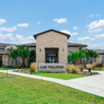 Entrance sign for Las Villitas residential community with a stone archway and landscaping under a bright sky (text reads 'LAS VILLITAS').