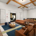 Open lobby lounge with brown leather sectional sofas, a round wooden coffee table, and a vaulted ceiling with exposed wooden beams.