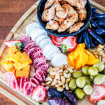 Charcuterie board with cheeses, fruits, olives, nuts, and a bowl of crispy fried chicken bites on top.