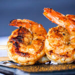 Skewers of grilled shrimp and chicken on a barbecue grill with charred, seasoned coating.