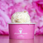 Scooped vanilla ice cream piled on a pink cup with a white logo, set against a pink blurred background (brand: phusecream).