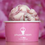 Close-up of a pink and vanilla swirled ice cream scoop in a pink branded cup with a white ice-cream cone logo.