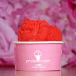 Red ice cream scoop perched in a pink cup against a soft pink floral background.