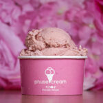 Pink ice cream scoops served in a pink branded cup against a pink flower backdrop, close-up.