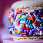 Close-up of a donut with a light glaze and multicolored sprinkles on a pink plate or background.