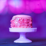 Close-up of a pink macaron on a white dessert stand, with a purple-pink bokeh background