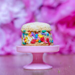 Cupcake with colorful sprinkles on a pink cake stand against a soft pink background