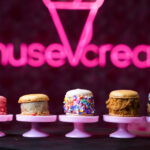 Colorful macarons on pink display stands with a pink neon sign blur in the background.