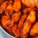 Pieces of fried chicken in a bright red, glossy sauce simmering in a pot