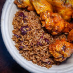 Brown rice with kidney beans beside orange-glazed fried chicken in a ceramic bowl