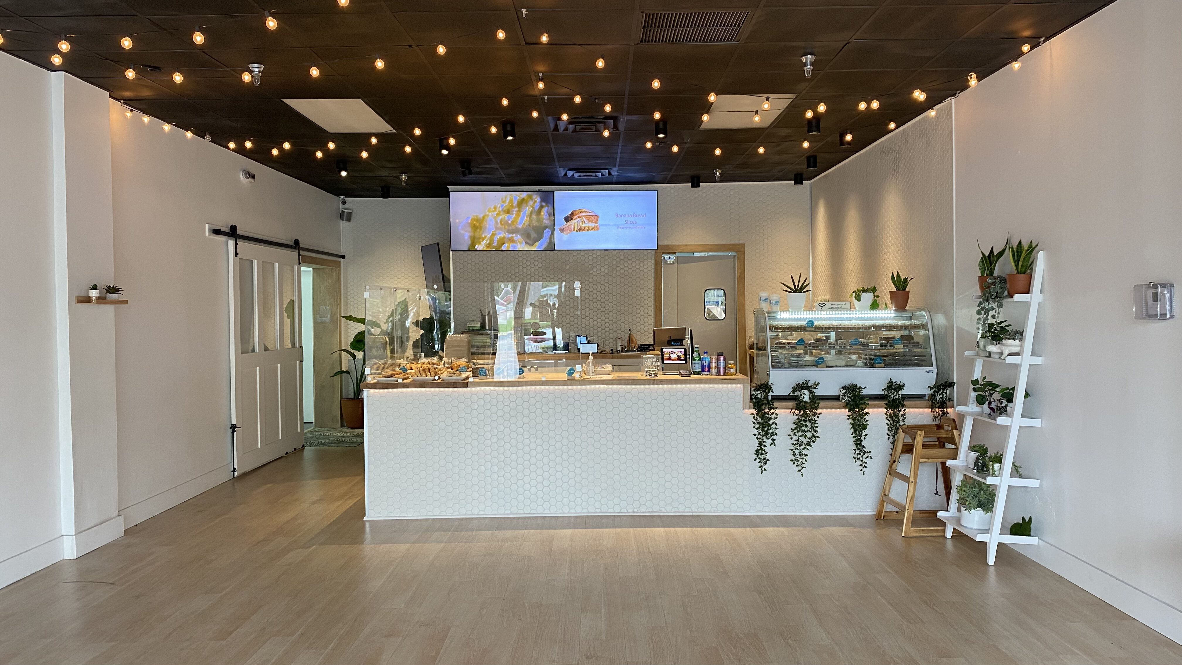 Bright cafe interior with a white hex-tiled counter, pastry display, and string lights overhead.