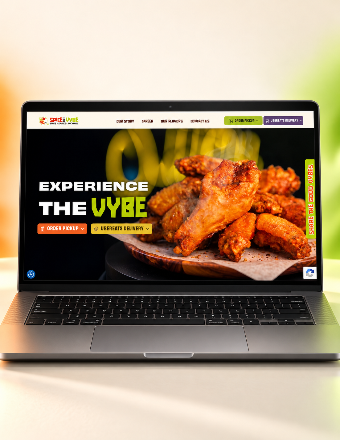 Laptop laptop screen displaying a spicy chicken wings promo with text 'EXPERIENCE THE VYBE' and order buttons on a black background, wings on a plate.